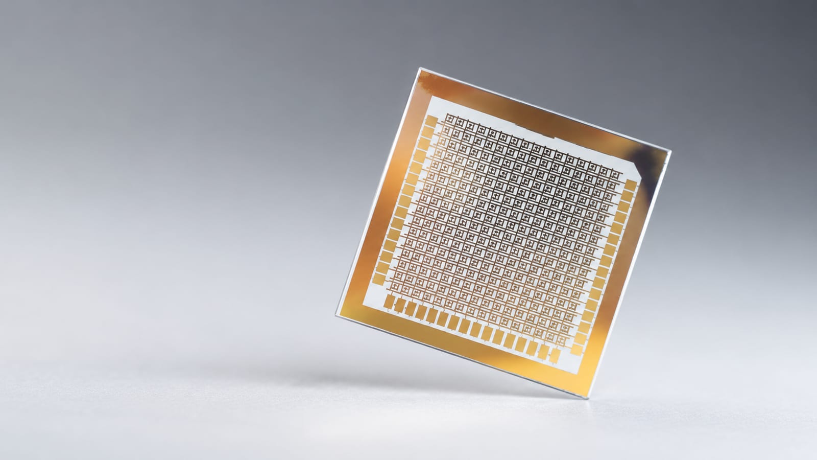 A small chip on a transparent substrate, held at an angle, with a gold-bordered grid of crossbar cells across its face.