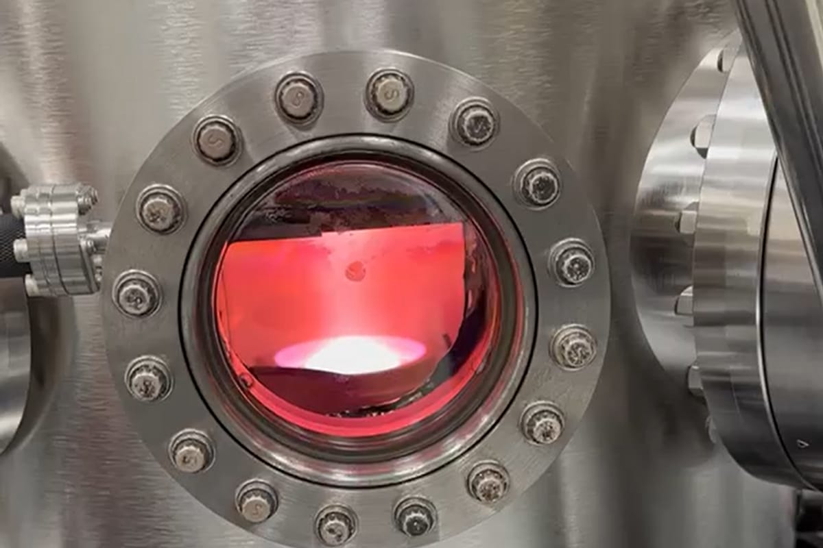 A vacuum chamber viewport glowing deep red from the heat inside.