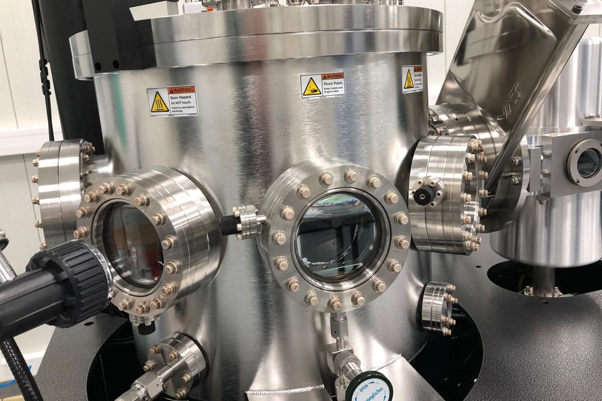 A stainless steel vacuum deposition chamber with bolted viewports and a gate valve on one side.